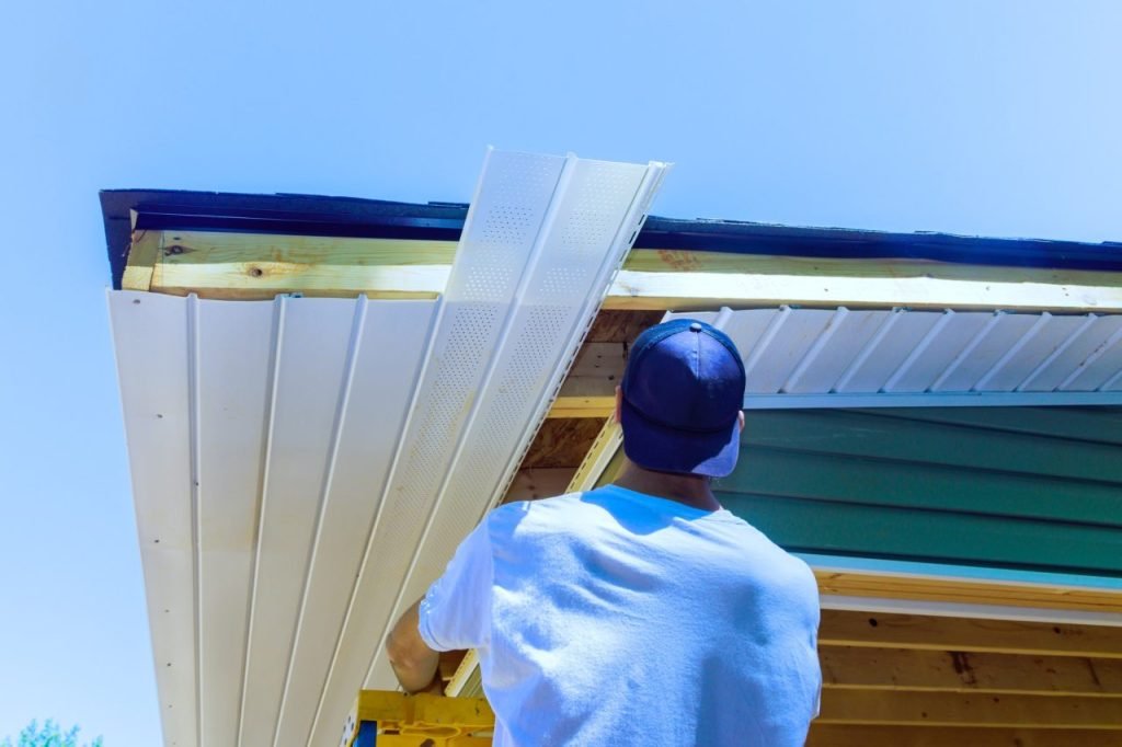 Tradesperson fitting white soffit boards beneath roof rafters