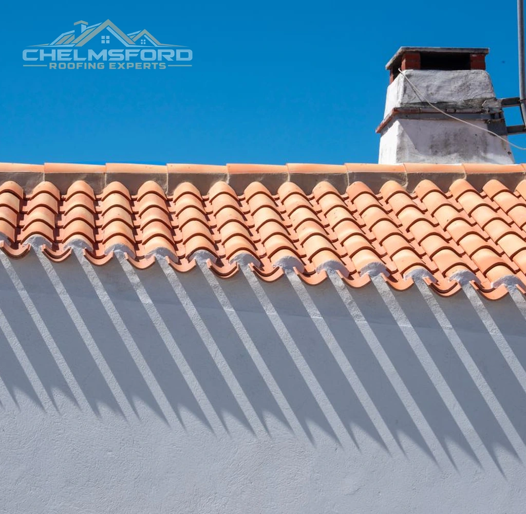 Clay tiled roof with chimney flashing against a clear sky