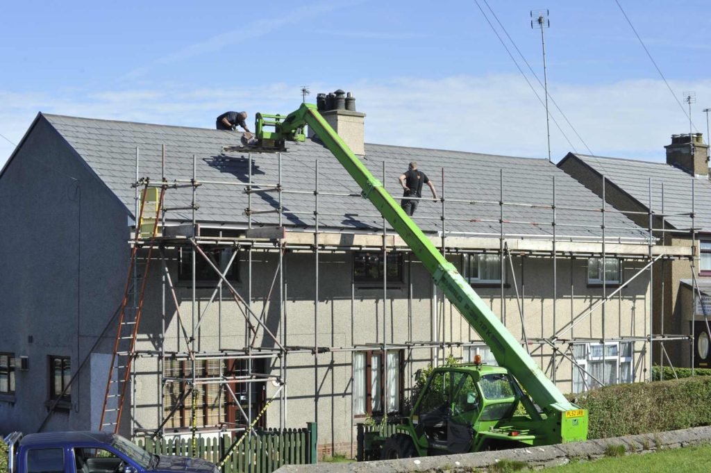 Slate roof replacement underway with scaffolding and a material lift