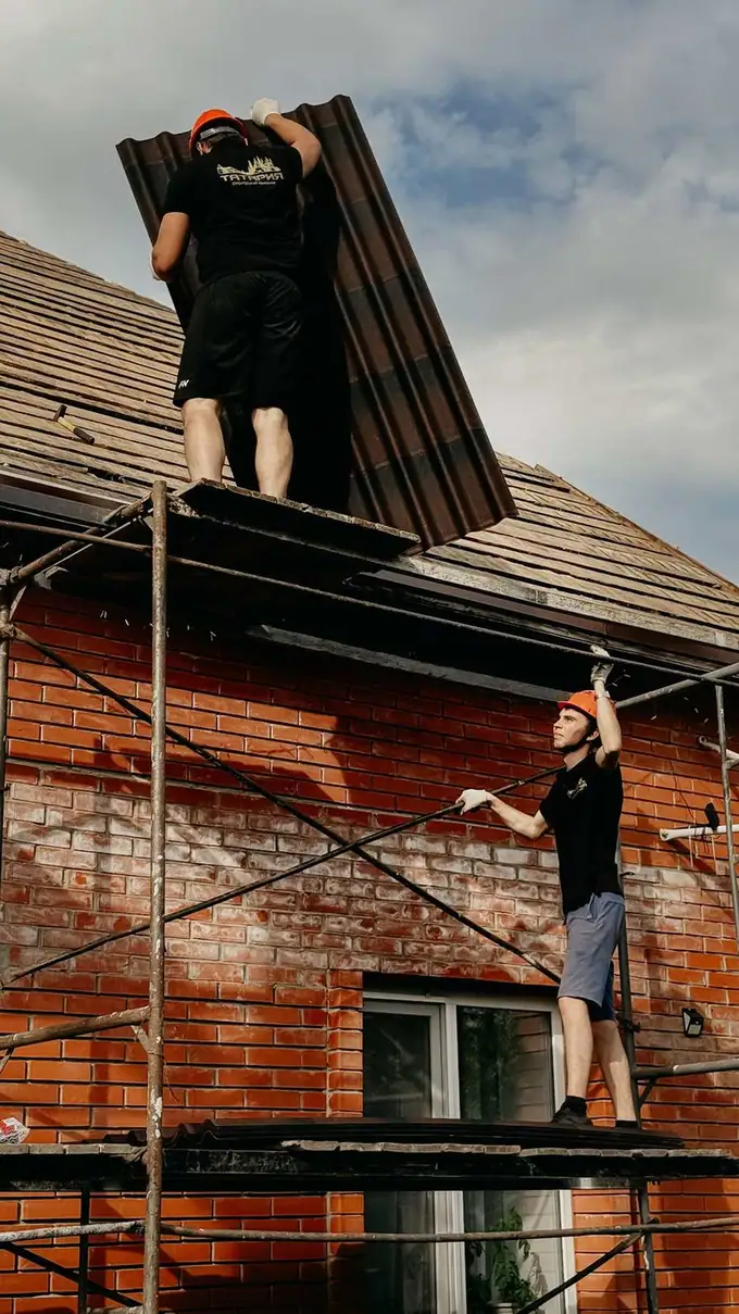 Roofers working beside the eaves of a tiled brick house