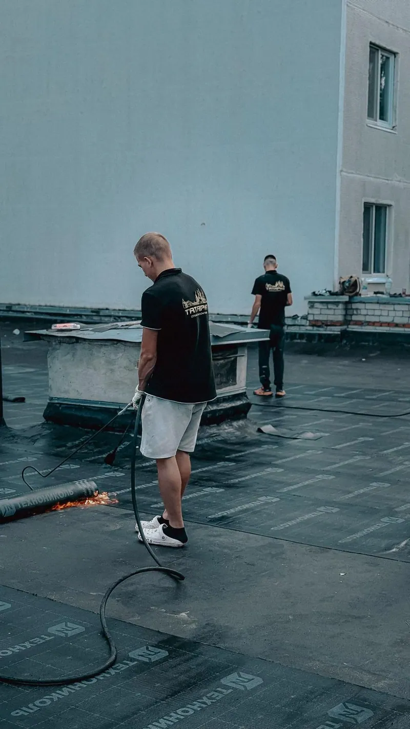 Roofers installing a dark flat roof beside a white building